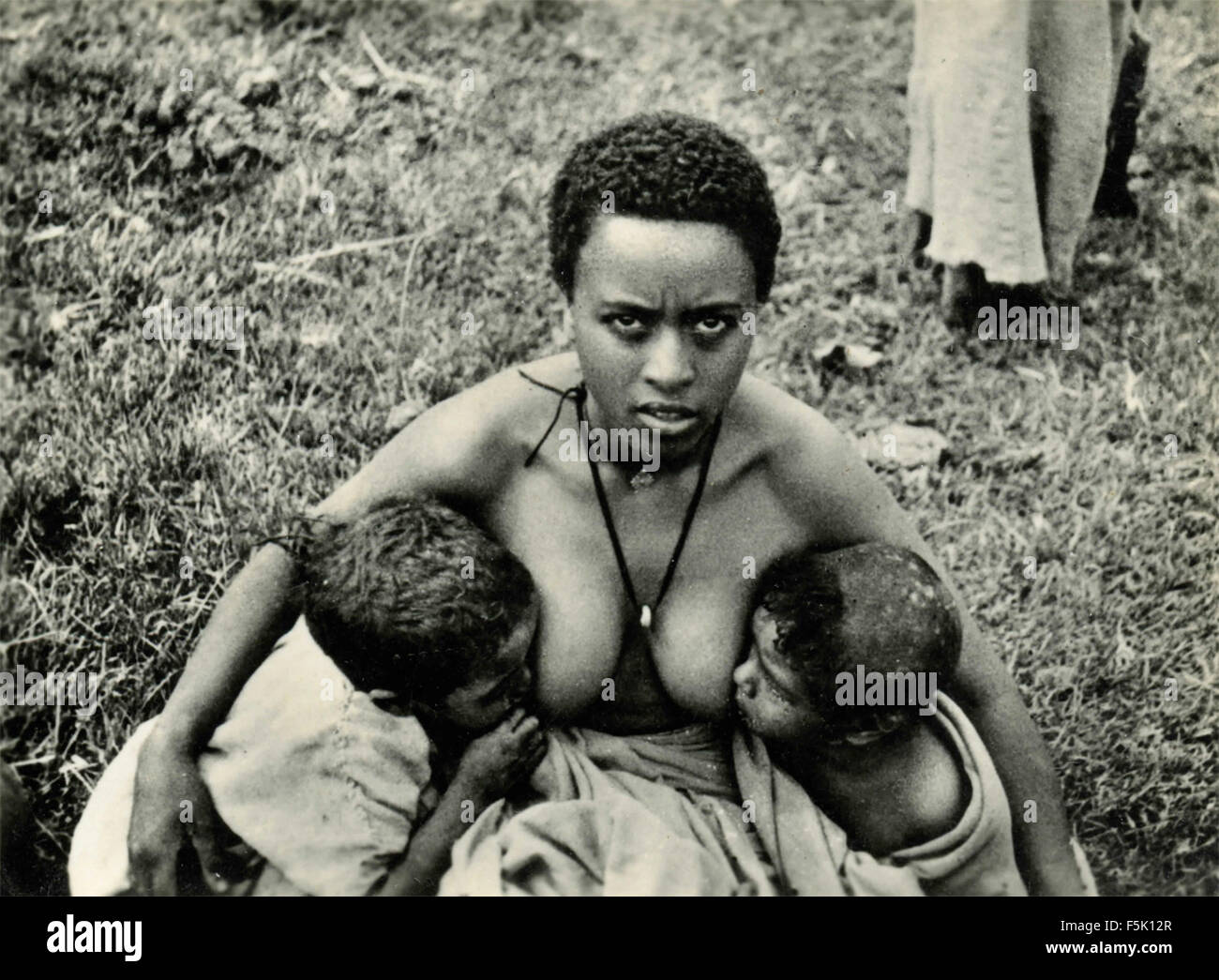 An African woman breast-feeding two big kids East Africa Stock Photo