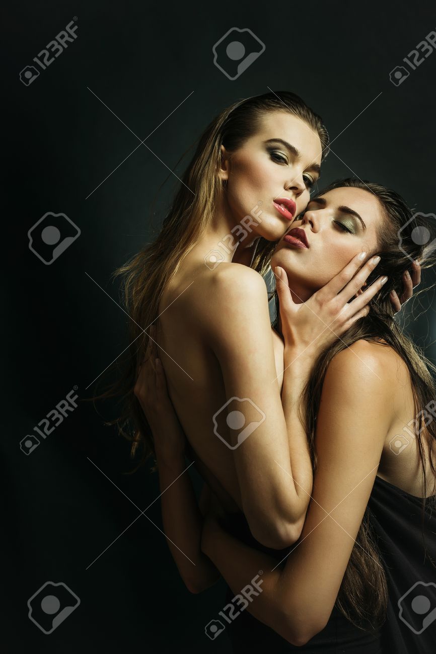 Love. Homosexual Couple Of Two Sexy Girls Or Pretty Women Fashionable Models With Beautiful Long Hair And Stylish Makeup Hugging And Kissing On Grey Background. Sexual Attraction To Sex Stock Photo Picture
