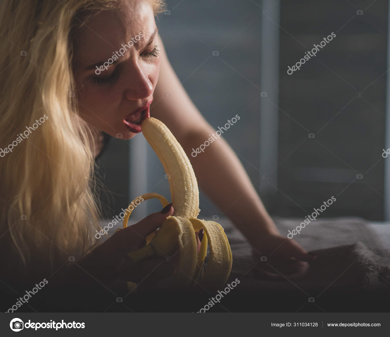 A girl with long blond hair looks sexy at a big banana. Opens her mouth and presents oral sex Stock Photo inside-studio 311034128