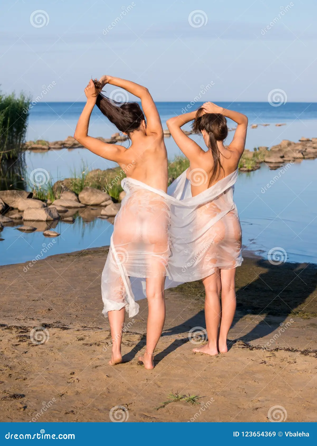 Two Young Nude Women Wrapped in White Shawl Posing on the Beach. Stock Image